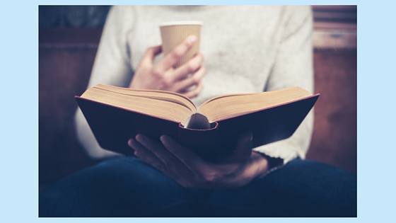 person holding a book and a cup of coffee
