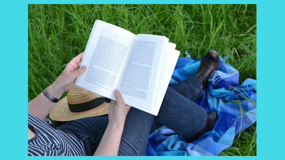 person reading in on a blanket in grass with straw hat on lap