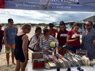 Beach goers browse through books at the Pop Up Library. Photo Courtesy of Rogers Memorial Library
