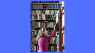 Photo of a child pulling a book from a shelf in a library
