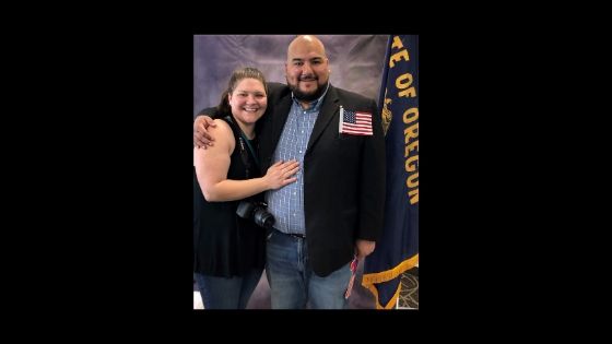 Two people posting for a photo one has a small american flag  