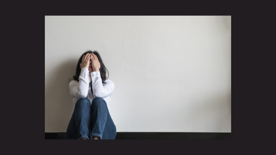 person sitting against a wall with head in hands