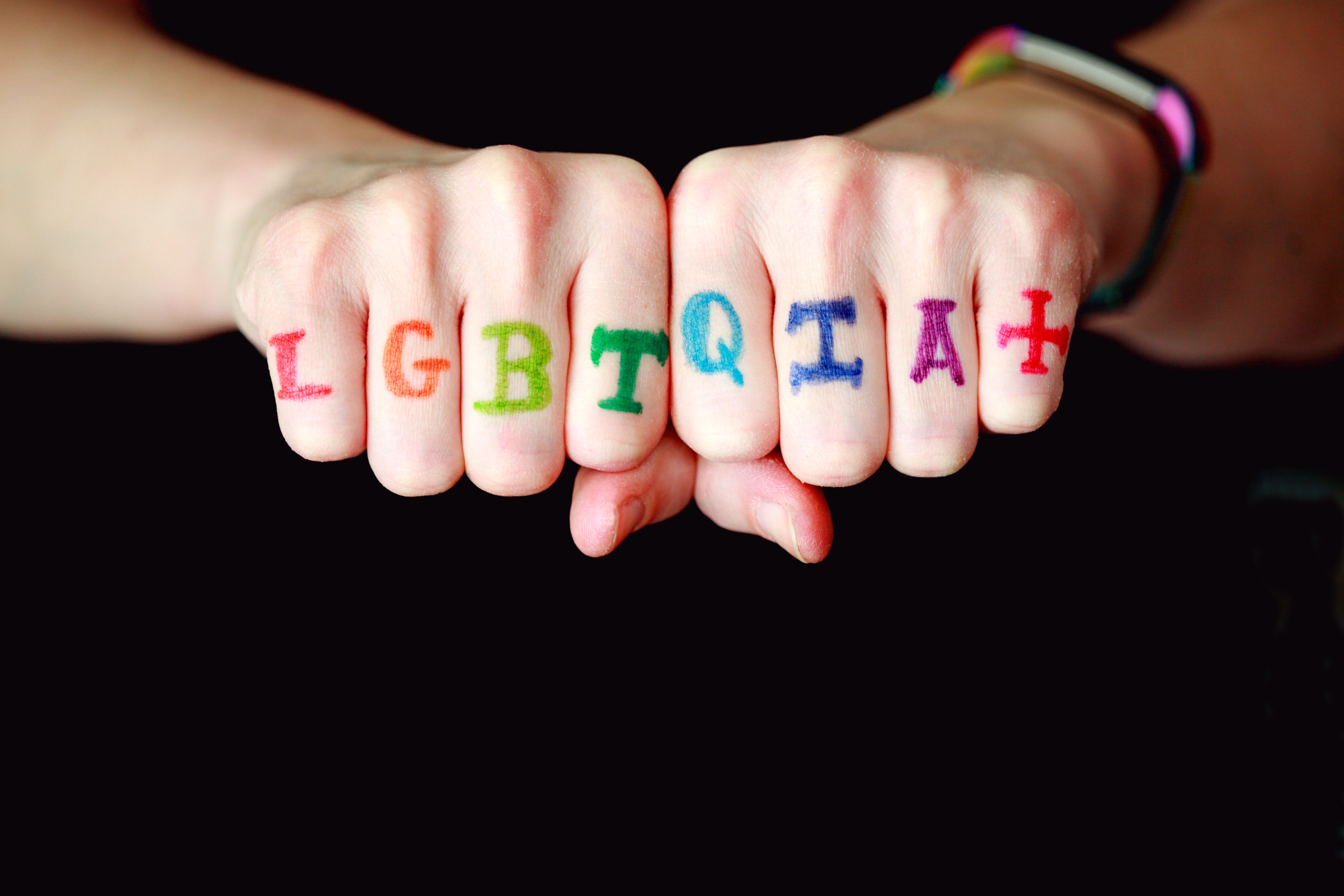 two fists with the letters LGBTQIA+ in rainbow colors on the fists