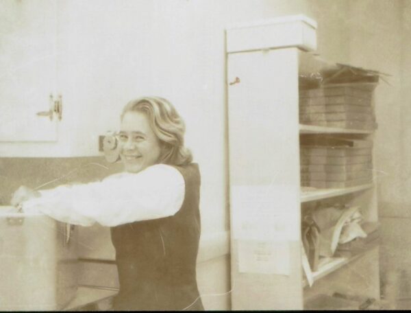 a woman with her hand in a box with a book shelf in background. vintage image black/white.