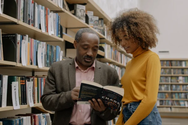 man and woman looking at a book together in front of library shelving