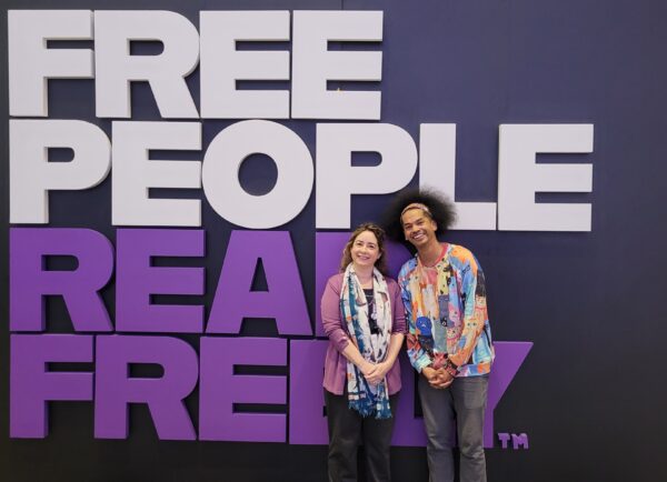 photo of two people Mychal Threets and the author in front of a wall that reads in white Free People and in Purple Read Freely - taken at the PLA 2024 conference