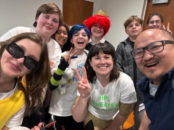 a group of people smiling at the camera teens and an adult in the middle giving the peace sign