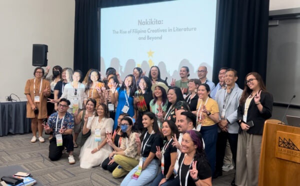 A group of Filipino and Asian American people pose with peace signs and smiles in front of a projector screen that reads "Nakikita: The Rise of Filipino Creatives in Literature and Beyond".