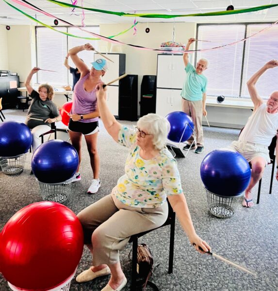 photo of people sitting on chairs in front of exercise or standing and holding drumsticks