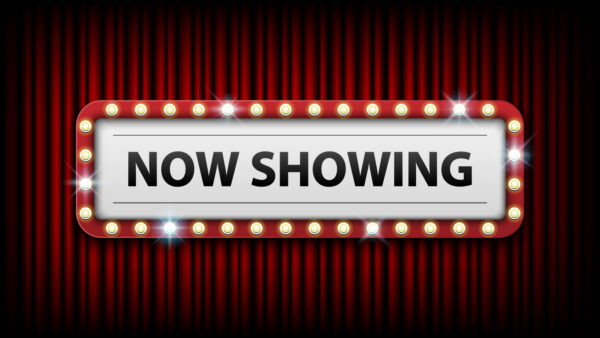 red curtains in background, white sign in lights, black letters that spell "Now showing"